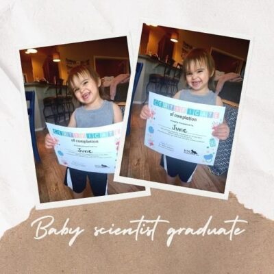 Toddler girl standing in gray shirt holding a certificate