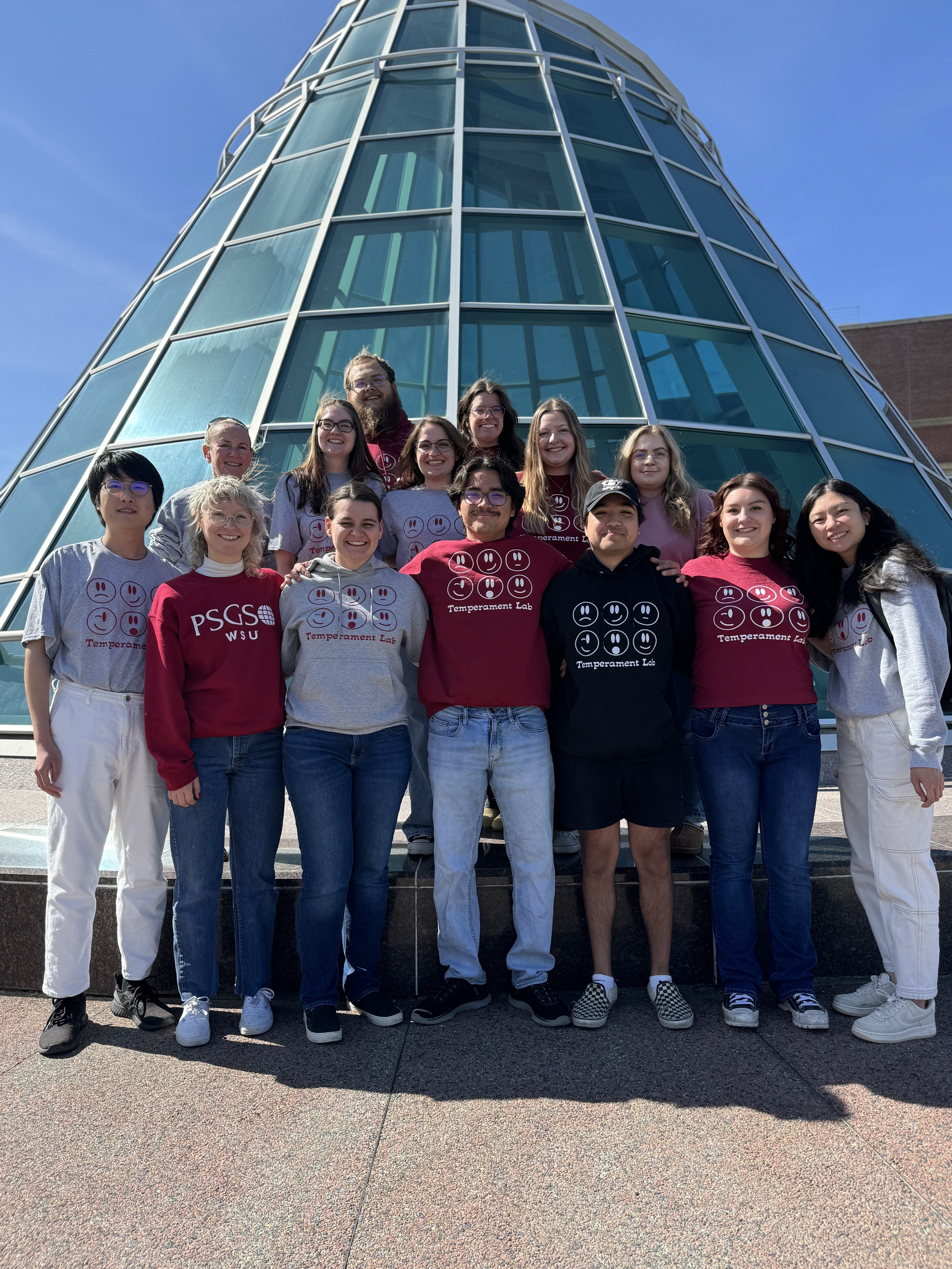 Group of research students and faculty standing in front of large window-paned tower.