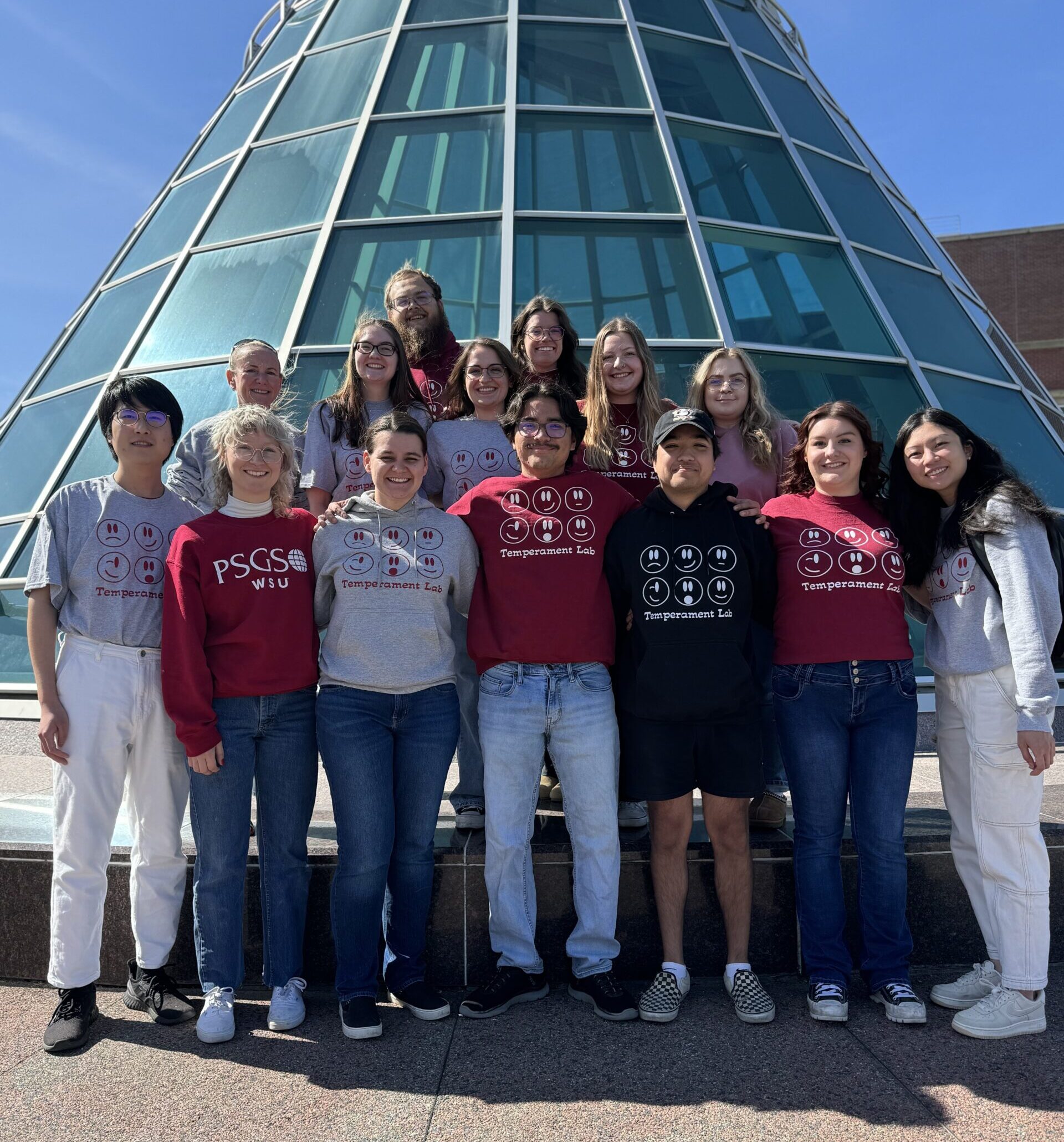 Group of research students and faculty standing in front of large window-paned tower.