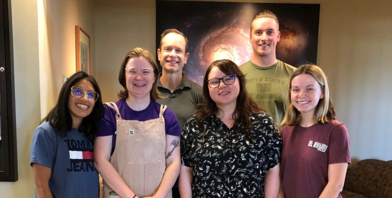 McCluskey group members standing in front of an astrophysics poster. L to R: Macarena, Lauren, Matt, Cassi, Cody, Julie