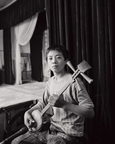 The performers are usually accompanied by a small group of musicians. Here a boy plays a sanxian, a traditional three stringed instrument.