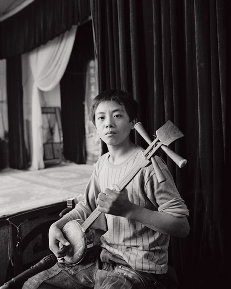 The performers are usually accompanied by a small group of musicians. Here a boy plays a sanxian, a traditional three stringed instrument.