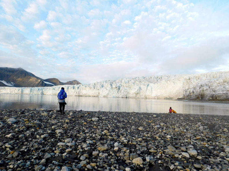 Standing on rocky shore of Svalbard, person looks at a glacier. Photo Debbie Lee