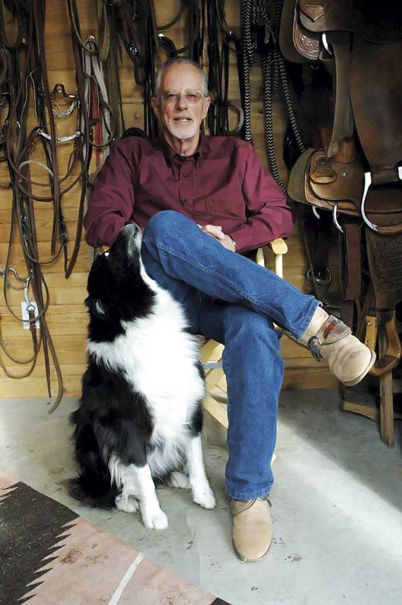 Don Weller seated with his dog at home in front of bridles and saddles