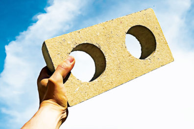 Hand holds drywall waste block against sky background