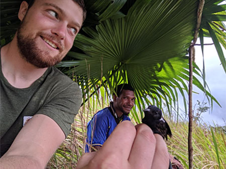 Man holding a bird under a leaf shelter