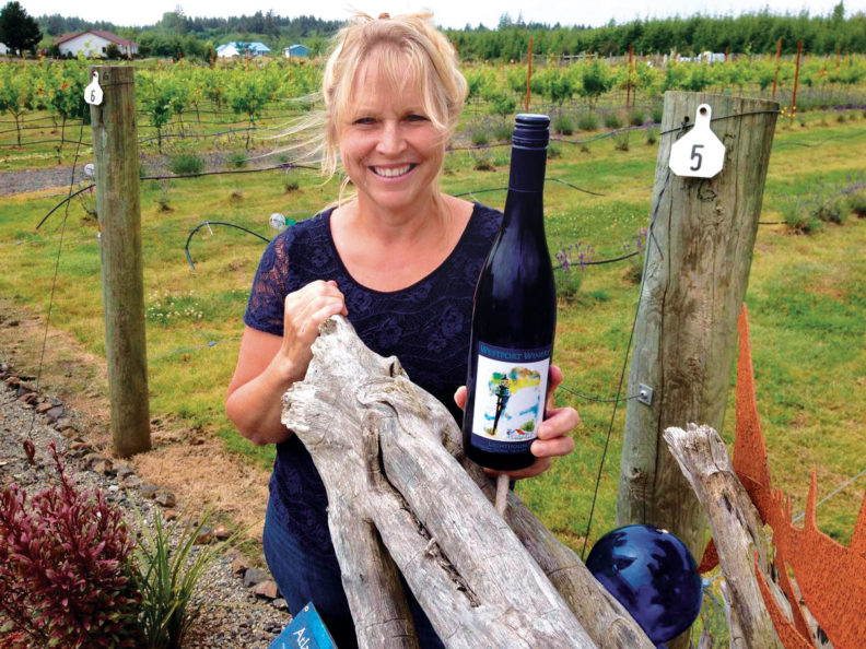 Kim Roberts from Westport Winery stands in front of the vineyard with a bottle