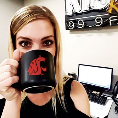 Taryn Daly drinks coffee from her WSU Coug head mug in front of radio equipment