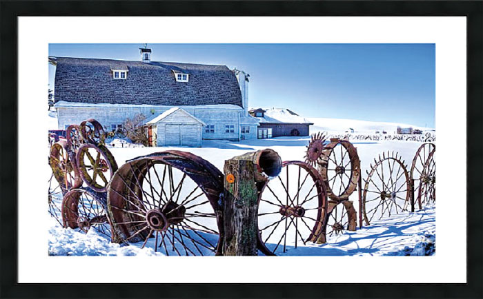 Photo of fence made of old metal wheels in front of a barn in snow