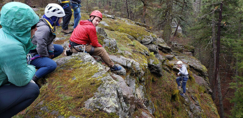Group of young people in helmets rock climbing in a forest