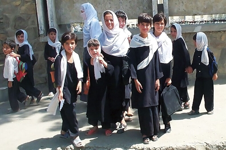 A group of children dressed in black with white shawls look toward the camera.