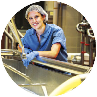 Sarah Beale, head cheesemaker at Washington State University Pullman, wears haircap, blue gloves and blue work clothes as she stand in creamery
