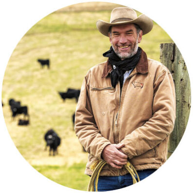 Brent McCann at Washington State University in a hat and coat holds a rope. In the background are cattle.