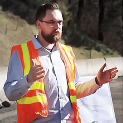Engineer Riley Bender wearing safety vest gestures next to a road