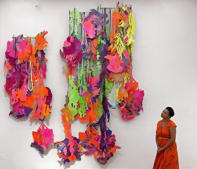 Colorful multimedia art hangs on wall as Io Palmer looks at it