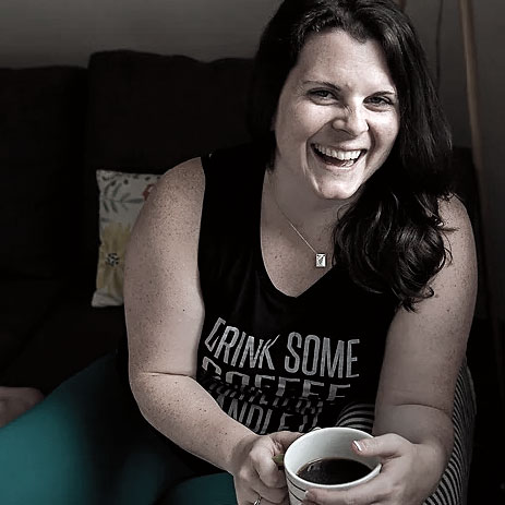 Ellyn Schinke laughs, holding a coffee cup while sitting on a sofa
