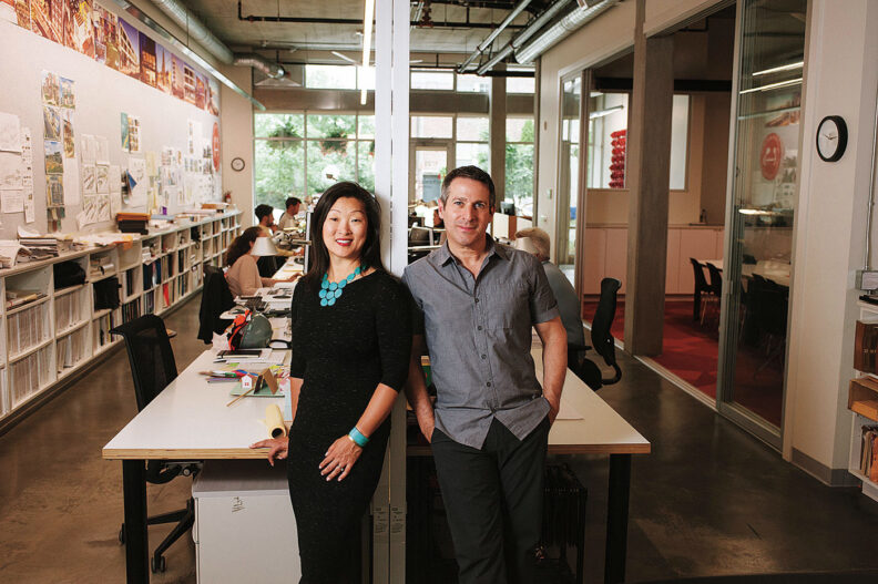 Grace Kim and Mike Mariano in front of a long table and the office space at Schemata Workshop