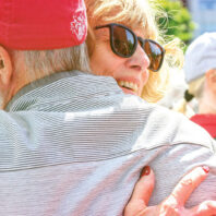 Woman in sunglasses hugs man wearing WSU baseball cap