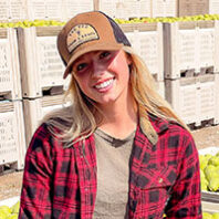 Kaitlyn Thornton in baseball cap, flannel shirt and jeans in front of crates of pears