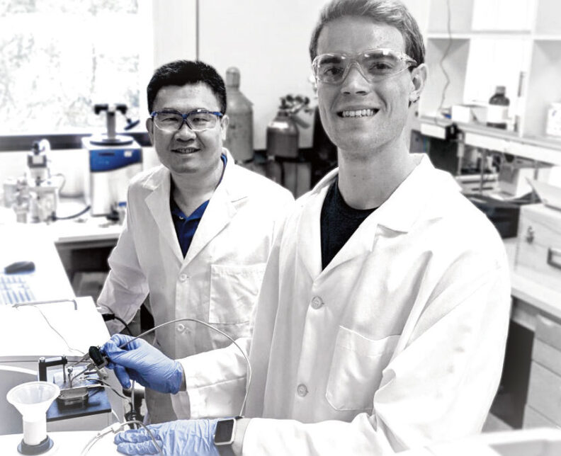 Two men in lab coats and safety glasses in a lab