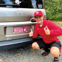 Man in WSU hat and shirt gives two thumbs up in front of his WSU-themed license plate