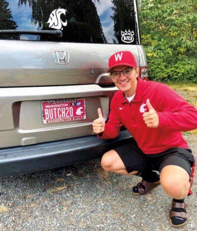 Man in WSU hat and shirt gives two thumbs up in front of his WSU-themed license plate