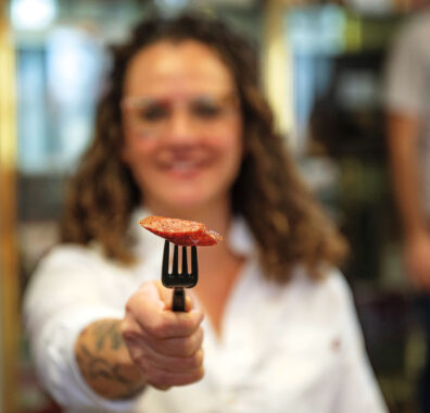 A woman holds out a piece of sausage on a fork