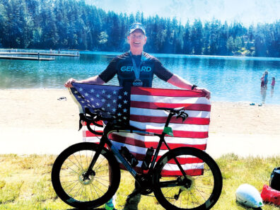 Mike McQuaid holds an American flag behind his bike at a triathlon