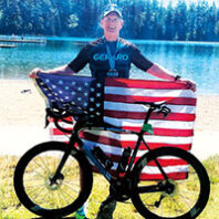 Mike McQuaid holds an American flag behind his bike at a triathlon