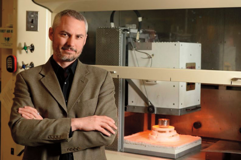 John McCloy stands in a lab in front of scanning equipment