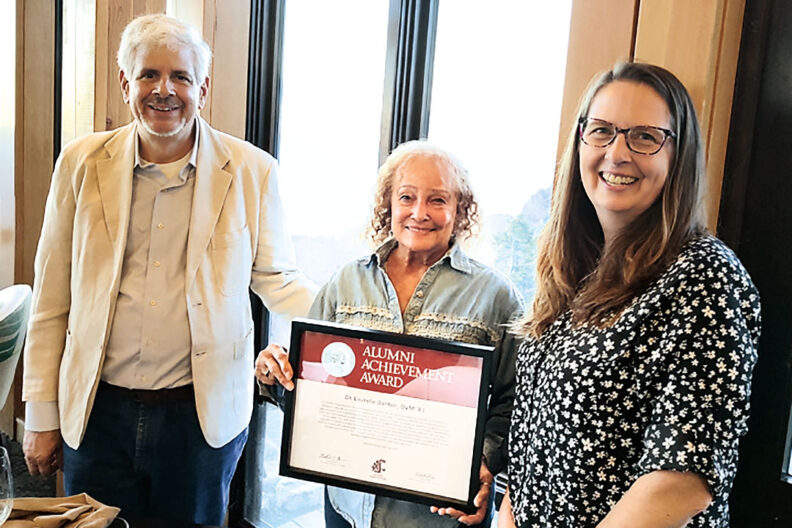 Laurelle Danton holds up WSU Alumni Achievement Award between two people