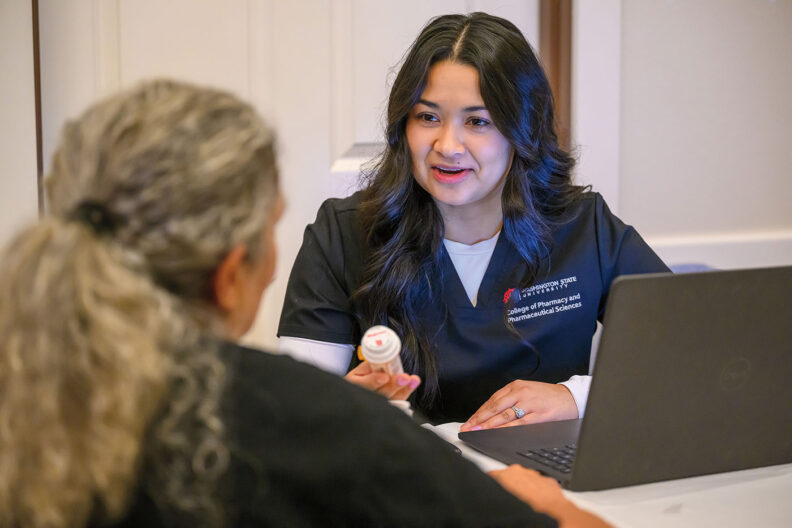 Woman pharmacy student holds a bottle of pills as she talks to another woman