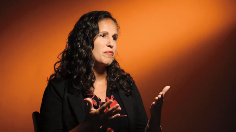Celestina Barbosa-Leiker speaking in front of an orange background