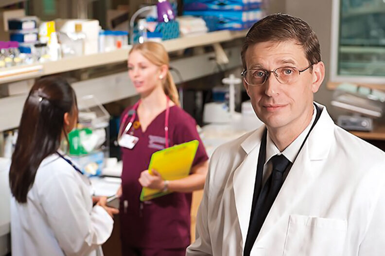 John Roll in a lab with two women in the background talking