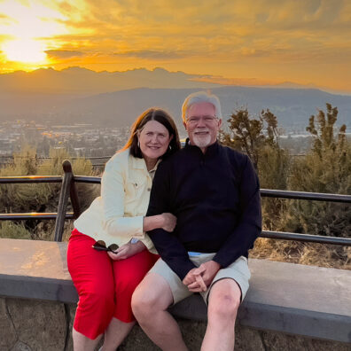Older man and woman in front of forested landscape at sunset