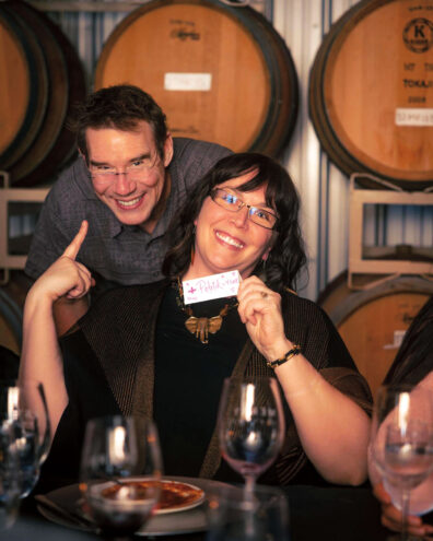 Smiling man and woman in front of wine barrels