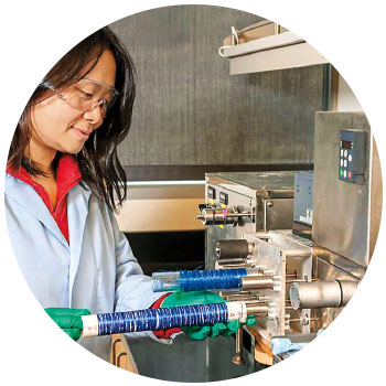 Woman in safety glasses in lab looks at fibers on long spool