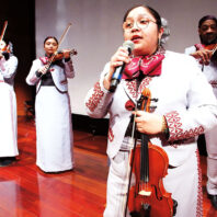 Woman holding a violin sings mariachi songs with a band playing behind her
