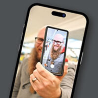 Bearded man holds a phone showing himself, framed in a smartphone