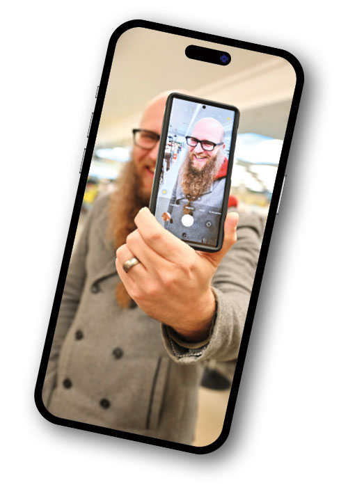 Bearded man holds a phone showing himself, framed in a smartphone