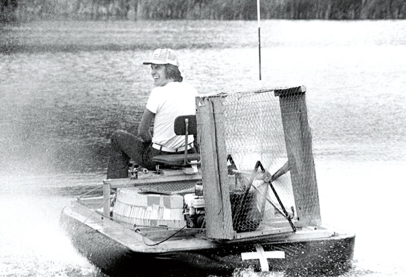 Laughing man in cap riding a homemade hovercraft on a pond