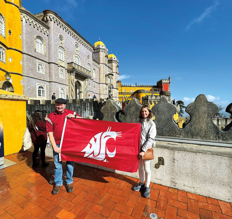 An older man and his daughter hold the WSU flag in front of old buildings in Portugal