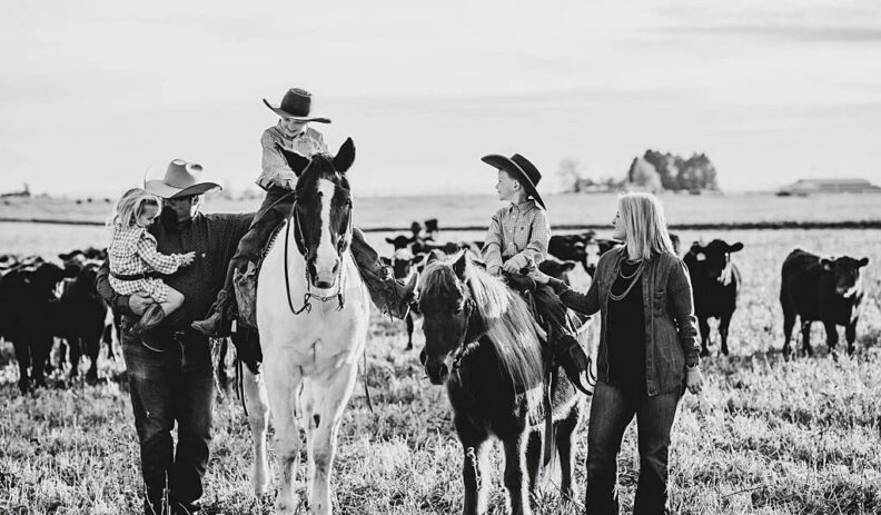 Man in cowboy hat holds little girl, two small boys in cowboy hats on horses, and woman holds one of the horses