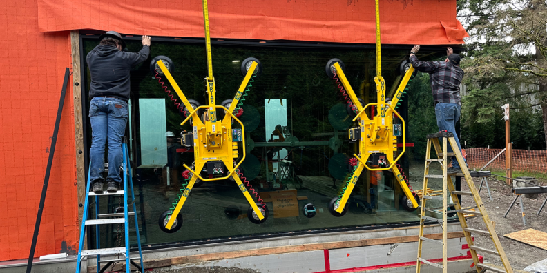Suction cup arms hold a large window for two men on ladders