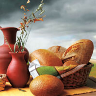 Photoillustration of bread in a basket, vases, with a gray sky and green field background