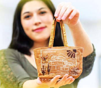 A young woman holds a small brown handbag made of dried kombucha with Southwestern design
