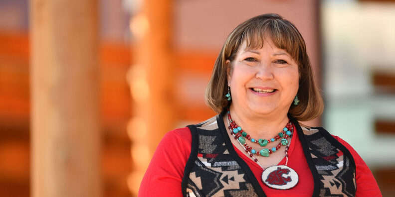 Smiling woman wearing Northwest Native American style vest and WSU logo necklace