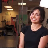 Woman, smiling in a black shirt, being interviewed in a TV studio
