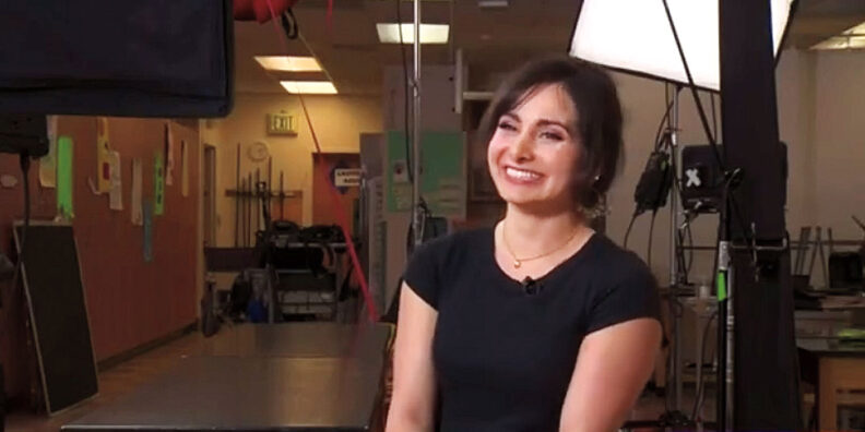 Woman, smiling in a black shirt, being interviewed in a TV studio