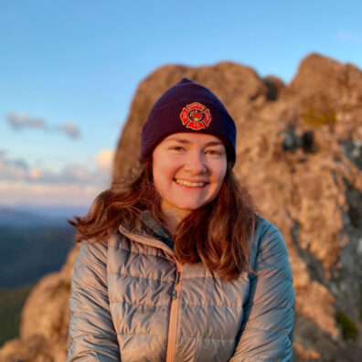 Woman in a stocking cap and winter coat sits by a rocky shore